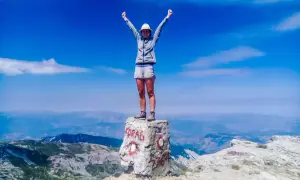 Szczyt Korab zdobyty! Radosna turystka z rękami w górze na skale z napisem "KORAB" i wysokością 2764 m.