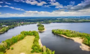Malownicze wyspy na bałtyku, otoczone ciemną wodą i bujną zielenią lasów, pod błękitnym niebem z chmurami.