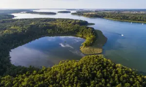 Malownicze wybrzeże szkierowe z lasami i jeziorami. Mała łódka na spokojnej wodzie, żaglówki na otwartym akwenie.