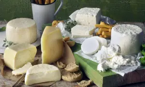 Różnorodne sery, w tym biała feta, żółte sery i świeży twaróg, podane z pieczywem i ziołami.