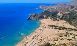 Widok na zatokę z turkusową wodą, piaszczystą plażą pełną leżaków i parasoli, wodnym placem zabaw. Jedna z najlepszych plaż w Grecji.