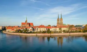 Wrocławskie katedry z zieloną iglicą i bliźniaczymi wieżami odbijają się w spokojnej wodzie Odry.
