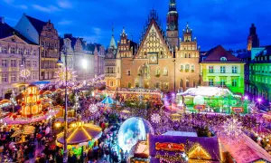 Tłoczny jarmark we Wrocławiu nocą, rozświetlony tysiącami lampek. Widać Ratusz, karuzelę i stragany.