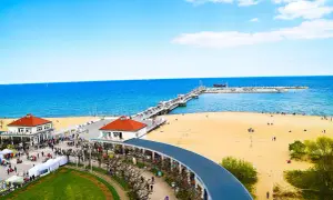 Słoneczna plaża w Sopocie z molo, budynkami i spacerującymi ludźmi.