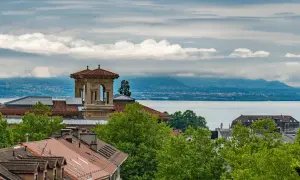 Widok na Jezioro Genewskie z dachu w Lozannie. W oddali góry, na pierwszym planie dachy i wieża.
