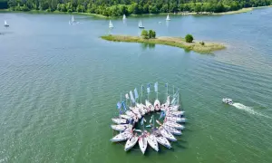 Piękne krajobrazy Polski: żaglówki tworzą okrąg na jeziorze, w tle las i mała wyspa.