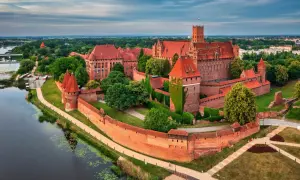 Malbork, największy zamek w Polsce, majestatycznie wznosi się nad rzeką Nogat. Czerwona cegła i strzeliste wieże tworzą imponujący widok.