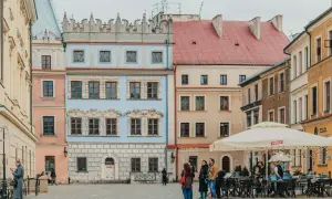 Kolorowe kamienice na Rynku Starego Miasta w Lublinie, z ludźmi spacerującymi i siedzącymi w ogródku kawiarnianym.