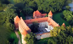 Zamek w Bytowie otoczony zielenią, z czerwonymi dachami i wieżami, wygląda jak z bajki.