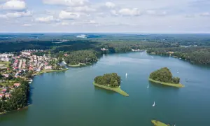 Malownicze jeziora w Polsce, z wyspami porośniętymi drzewami i żaglówkami na wodzie. W oddali widać lasy i zabudowania.