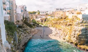 Słoneczna plaża w **Putignano** z białymi domami na klifach i turkusowym morzem.