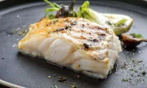 Usmażony filet ryby miruna z ziołami i warzywami na czarnym talerzu.