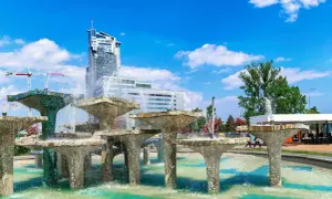 Fontanna z modernistycznymi budynkami w tle i błękitnym niebem.