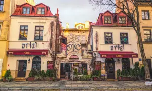 Urokliwe kamienice w krakowskiej dzielnicy żydowskiej, z szyldami "Ariel" i ozdobnym drzewem życia nad wejściem.