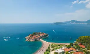 Sveti Stefan, Czarnogóra, z widokiem na turkusowe morze i zatłoczoną plażę.