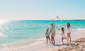 Rodzina cieszy się wczasy nad morzem z wyżywieniem dla rodzin z dziećmi, puszczając latawiec na piaszczystej plaży przy turkusowej wodzie.