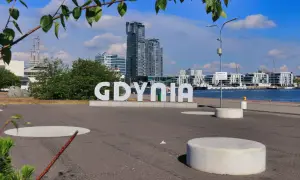 Napis "GDYNIA" na tle nowoczesnych budynków i żaglowca. Widok na port, idealny na spacer po gdynia stare miasto.