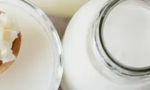 Ziarna żętycy na łyżce obok szklanki i butelki z mlekiem. To naturalny probiotyk.