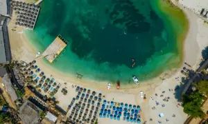 Widok z lotu ptaka na plażę w Albanii. Turkusowe morze, biały piasek, rzędy parasoli i leżaków, ludzie kąpiący się i opalający.
