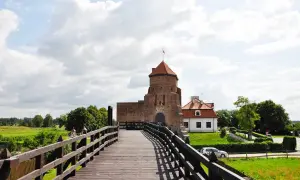 Drewniany most prowadzi do ceglanego zamku z czerwoną wieżą. To jedne z **ciekawych miejsc pod Warszawą**, idealne na wycieczkę.