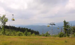 Kolejka linowa nad zielonymi zboczami Beskidu Śląskiego, z widokiem na kolejne szczyty w oddali.