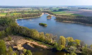 Malownicze jezioro z wyspami, otoczone lasami i polami. Idealne miejsce na romantyczne wypady w Polsce, gdzie można podziwiać przyrodę.
