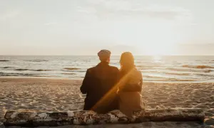 Para dwojga siedząca na pniu na plaży, patrząca na zachód słońca nad morzem. Idealne, fajne miejsce nad morzem dla dwojga.