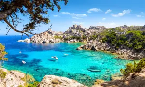 Turkusowa zatoka na Costa Smeralda, z łodziami i skalistymi brzegami porośniętymi zielenią.