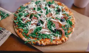 Pyszna pizza parma z rukolą, oliwkami i parmezanem, podana na papierze.