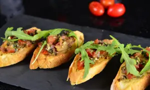 Cztery chrupiące **tapas** z pomidorami, ziołami i rukolą na ciemnej desce.
