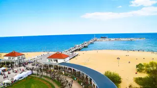 Słoneczna plaża w Sopocie z molo, budynkami i spacerującymi ludźmi.