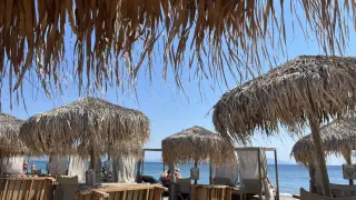 Słomiane parasole i leżaki na plaży Tigaki, z widokiem na spokojne, błękitne morze i bezchmurne niebo.