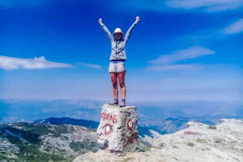 Szczyt Korab zdobyty! Radosna turystka z rękami w górze na skale z napisem "KORAB" i wysokością 2764 m.