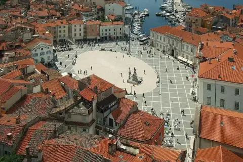 Widok na plac w Piran, Słowenia, z widokiem na morze i port. Czerwone dachy i zabytkowa architektura tworzą malowniczy krajobraz.