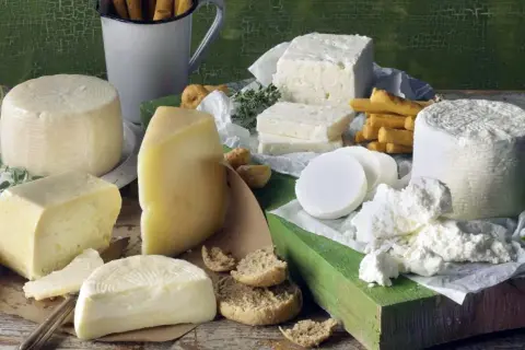 Różnorodne sery, w tym biała feta, żółte sery i świeży twaróg, podane z pieczywem i ziołami.