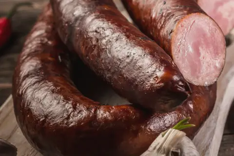 Kiełbasa lisiecka, wędzona, z widocznym przekrojem ukazującym różowe mięso. Obok czosnek i papryczka chili.
