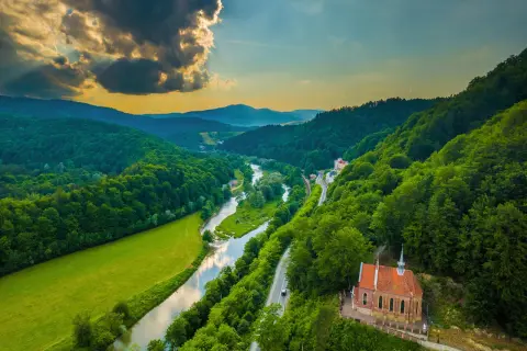 Malowniczy widok na Beskid Sądecki z rzeką, zielonymi wzgórzami i małą kapliczką.