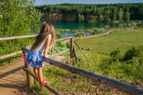 Dziewczynka na drewnianym pomoście podziwia turkusowe jezioro w Parku Gródek Jaworzno. Warto sprawdzić cenę wstępu, by cieszyć się tym widokiem.