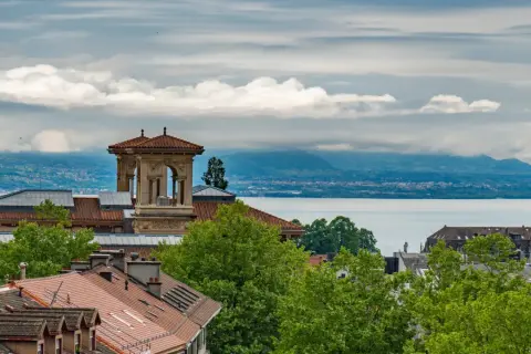 Widok na Jezioro Genewskie z dachu w Lozannie. W oddali góry, na pierwszym planie dachy i wieża.