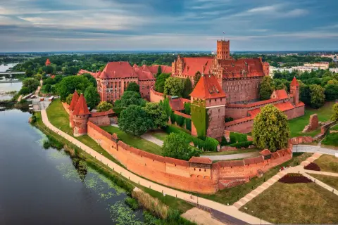 Malbork, największy zamek w Polsce, majestatycznie wznosi się nad rzeką Nogat. Czerwona cegła i strzeliste wieże tworzą imponujący widok.