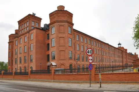 Imponujący, ceglany **księży młyn** w Łodzi, z charakterystycznymi wieżyczkami i długim rzędem okien. Obok znaki drogowe.