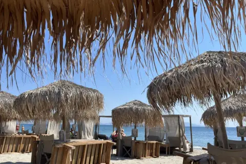 Słomiane parasole i leżaki na plaży Tigaki, z widokiem na spokojne, błękitne morze i bezchmurne niebo.
