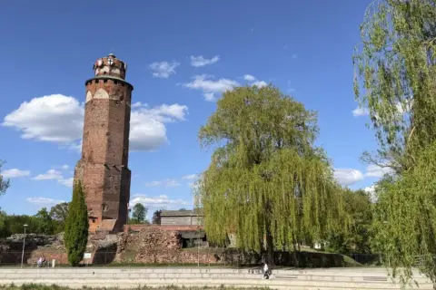 Wieża zamkowa w Brodnicy, otoczona zielenią, na tle błękitnego nieba z chmurami. Piękny dzień na Pojezierzu Brodnickim.
