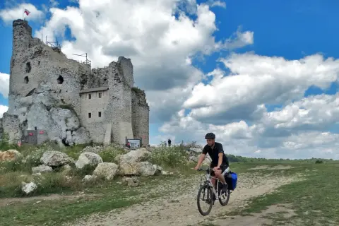 Rowerzysta przemierza malownicze **Jura Krakowsko-Częstochowska szlaki**, mijając ruiny zamku na skale.