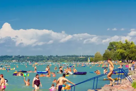Tłum ludzi cieszy się latem na **jeziorze Balaton**. Kąpiel, pływanie na materacach i relaks na plaży.