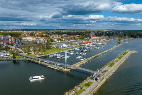Widok na jezioro, nad którym leży Giżycko, z mariną pełną łodzi, nowoczesnym mostem i spacerowiczami.