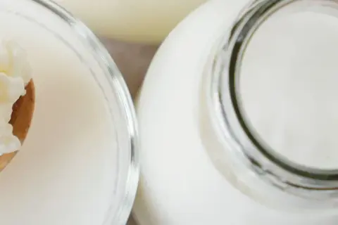 Ziarna żętycy na łyżce obok szklanki i butelki z mlekiem. To naturalny probiotyk.