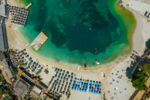 Widok z lotu ptaka na plażę w Albanii. Turkusowe morze, biały piasek, rzędy parasoli i leżaków, ludzie kąpiący się i opalający.