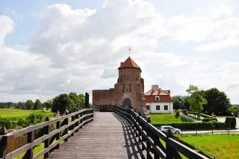 Drewniany most prowadzi do ceglanego zamku z czerwoną wieżą. To jedne z **ciekawych miejsc pod Warszawą**, idealne na wycieczkę.
