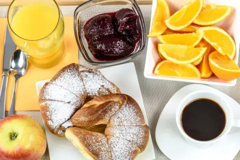 Idealne śniadanie kontynentalne: świeże croissanty, sok pomarańczowy, kawa, owoce i dżem.